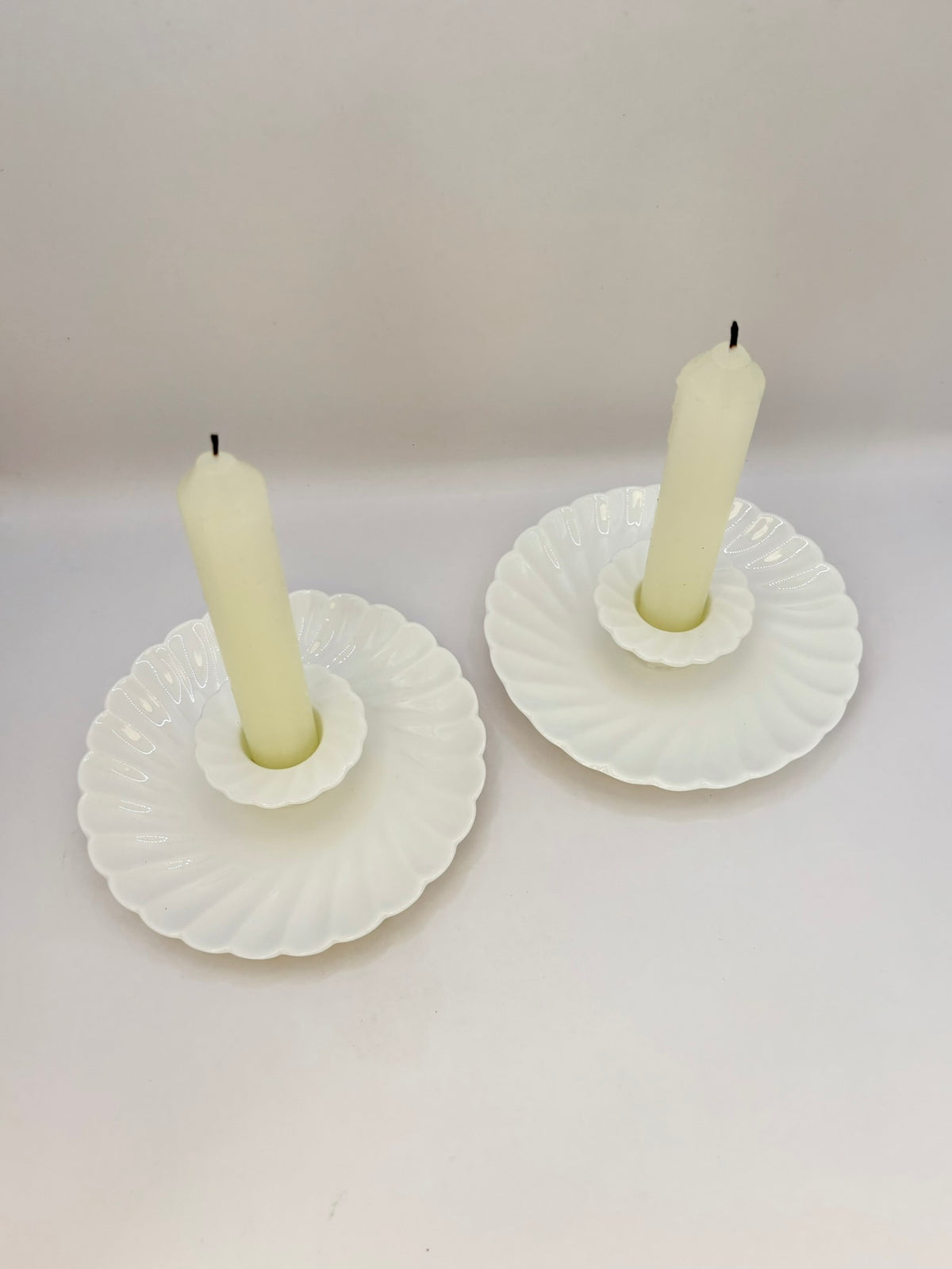 Two white shell-shaped candle holders with candles on a light gray background