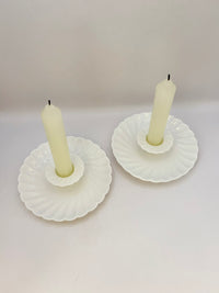 Two white shell-shaped candle holders with candles on a light gray background