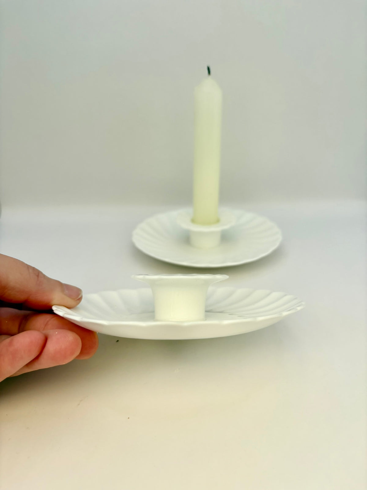 White candle on a decorative plate with a hand holding another plate underneath.