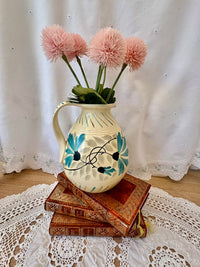 Decorative pitcher with pink flowers on a stack of books against a white curtain background