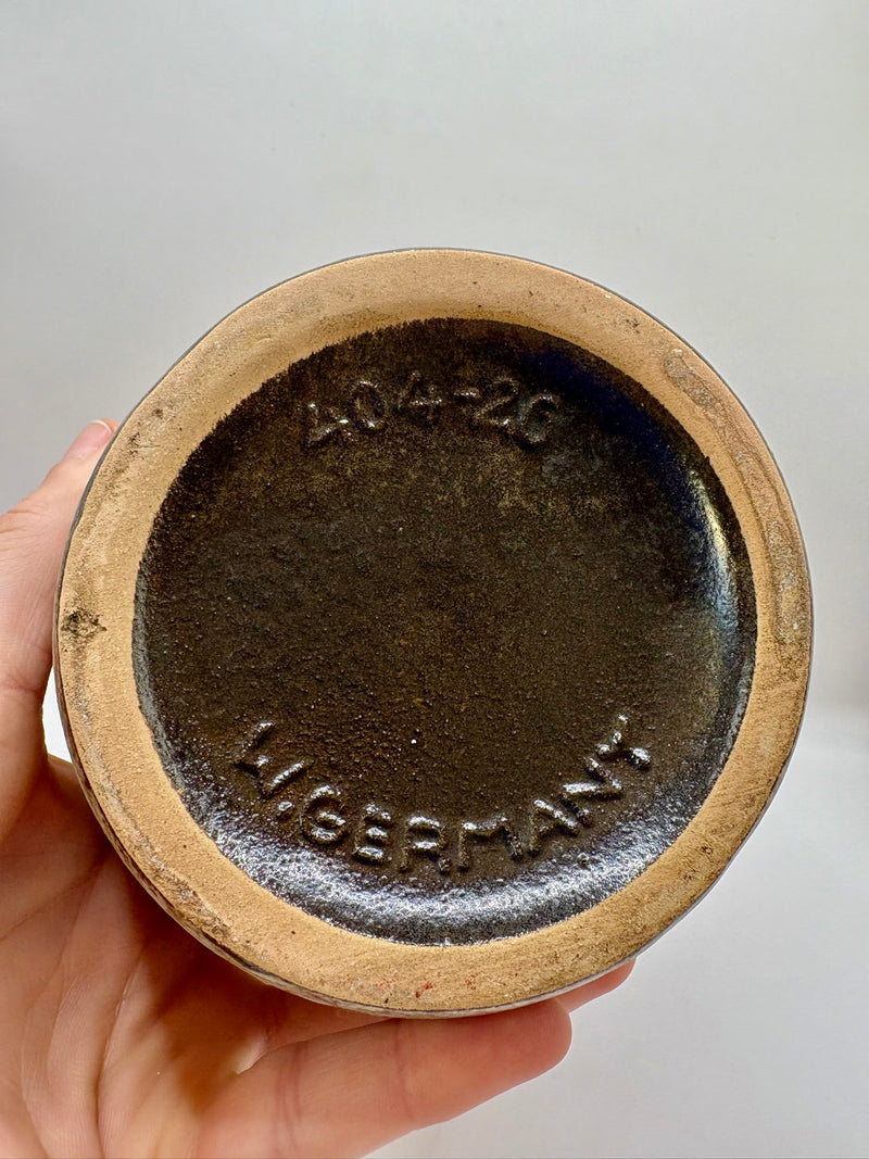 Hand holding a ceramic jar lid with 'W.Germany' branding on a brown background