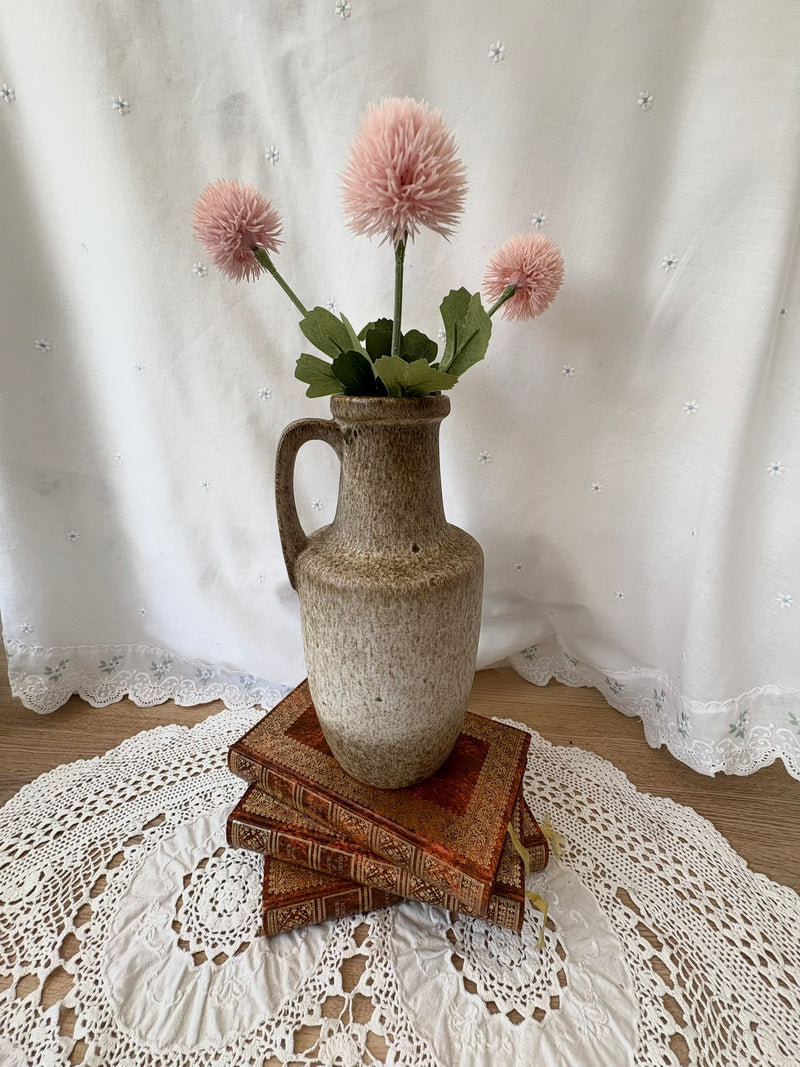 Vintage vase with pink flowers on a stack of books on a lace tablecloth