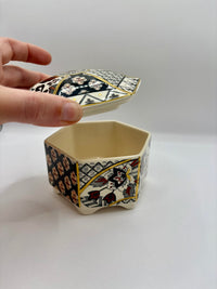 Decorative hexagonal box with a patterned lid held by a hand on a white background