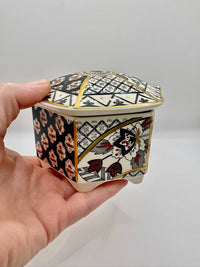 Decorative hexagonal box with intricate patterns held by a hand against a plain background