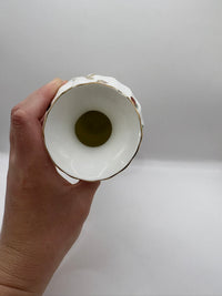 Hand holding a white ceramic vase with gold rim against a plain background