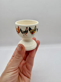 Hand holding a ceramic egg cup with chicken design on a plain background