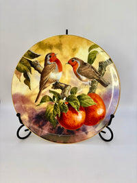 Decorative plate with two birds and apples on a stand against a white background