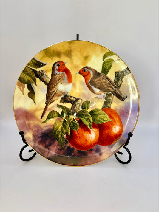 Decorative plate with two birds and apples on a stand against a white background