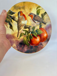 Decorative plate with bird and fruit design held by a hand on a white background