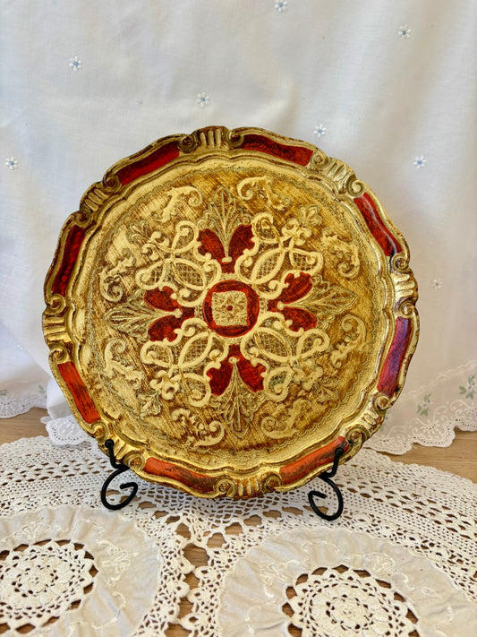 Decorative gold and red plate on a stand with a white lace tablecloth background