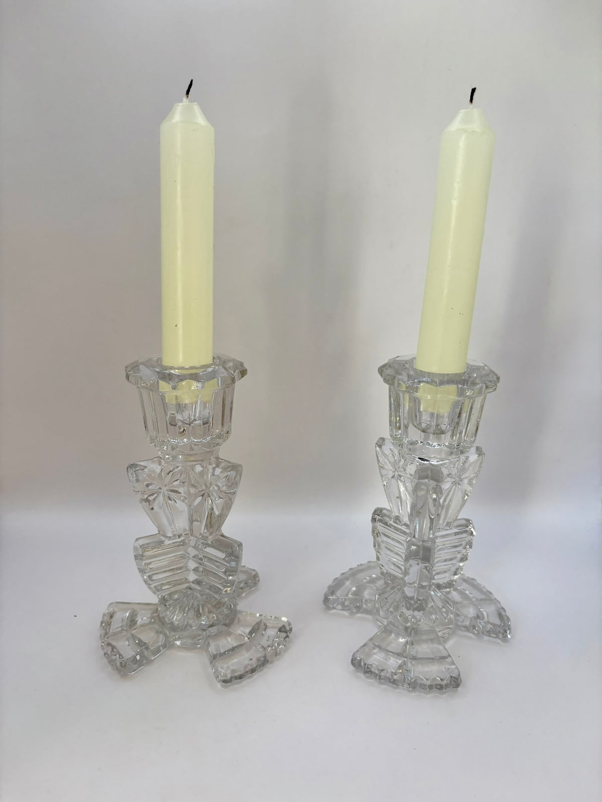 Two crystal candle holders with white candles on a plain background