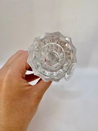 Clear glass knob held by a hand against a plain background
