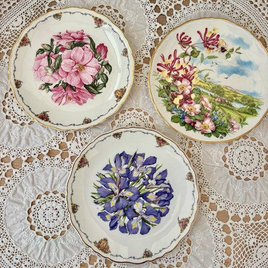 Three decorative plates with floral designs on a lace tablecloth.