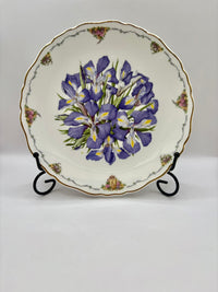 Decorative plate with purple floral design on a stand against a white background