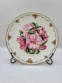 Decorative plate with pink floral design on a stand against a white background