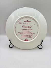 White plate with 'Royal Albert' and 'Camellia' text on a stand against a gray background