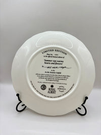 White decorative plate with text and branding on a stand against a white background