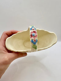 Hand holding a ceramic basket with colorful pattern on a plain background