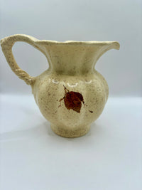 Beige ceramic pitcher with a brown stain on a white background