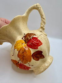 Ceramic pitcher with leaf designs on a white background