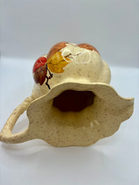 Ceramic birdhouse with a lid featuring a red and yellow leaf design on a white background