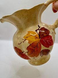Ceramic pitcher with autumn leaf design held by a hand against a white background