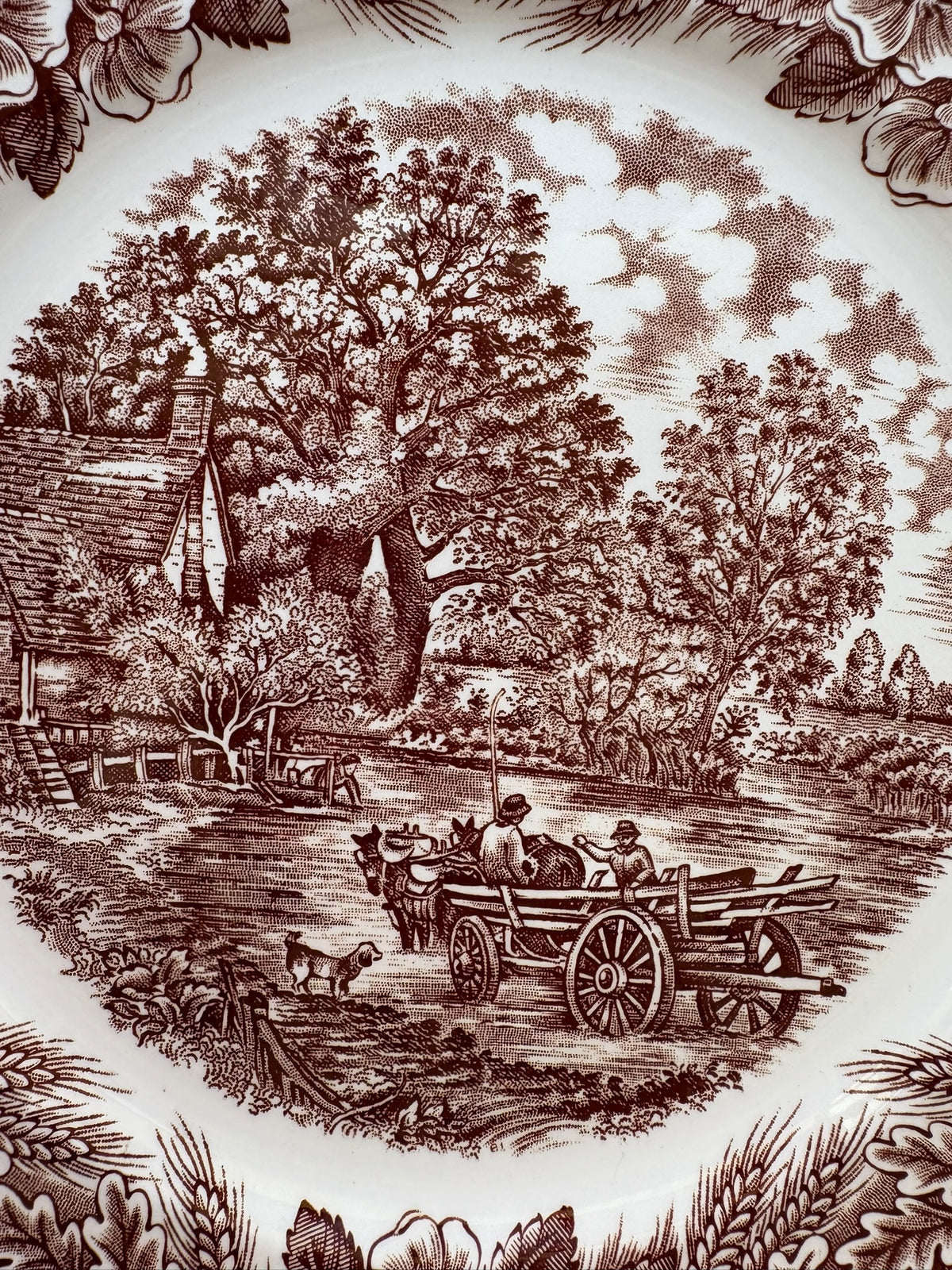 Vintage-style illustration of a rural scene with a cart and people, surrounded by trees and buildings.