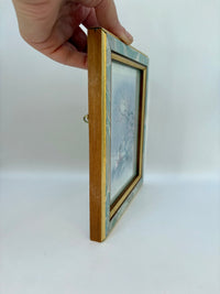 Hand holding a gold picture frame with a white background