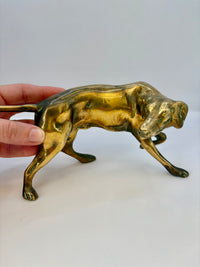 Brass panther figurine held by a hand on a white background