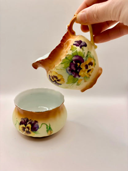 Ceramic teapot with floral design being held above a matching teacup on a white background