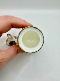 Hand holding a small ceramic cup with a white interior on a plain background