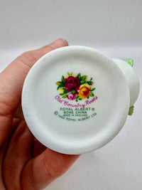 Hand holding a white ceramic container with floral design and 'Royal Albert' branding.