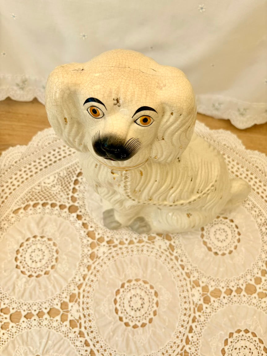 White ceramic dog figurine with black eyes and nose on a lace doily