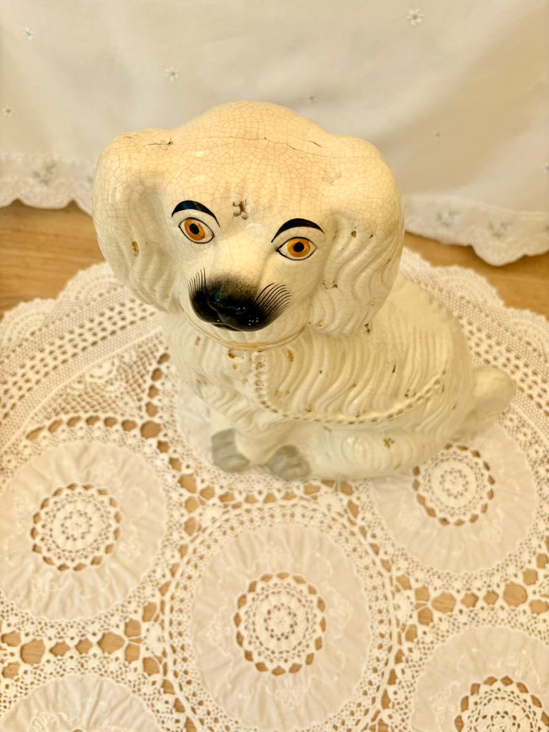 White ceramic dog figurine with black eyes and nose on a lace doily