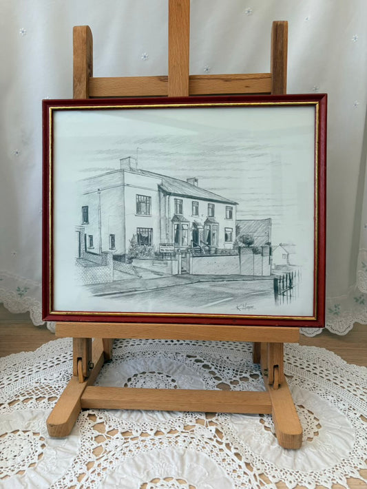 Pencil drawing of a house on an easel with a wooden frame.