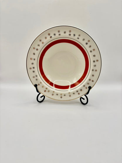 Decorative plate with red rim and starburst pattern on a stand against a white background