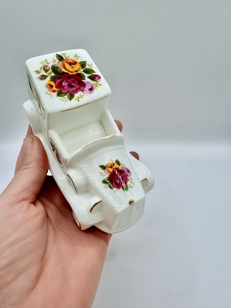 Small white ceramic car with floral designs held in a hand against a gray background