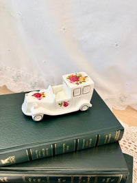 Decorative white car-shaped box with floral designs on a stack of books.