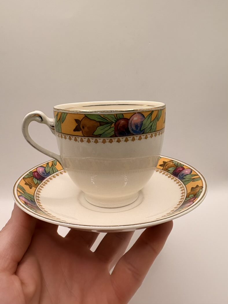 Teacup and saucer with decorative rim held by a hand against a plain background