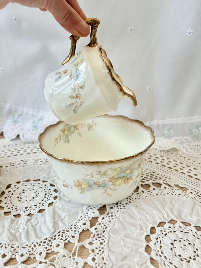 Vintage-style teacup and saucer with floral patterns on a lace tablecloth.