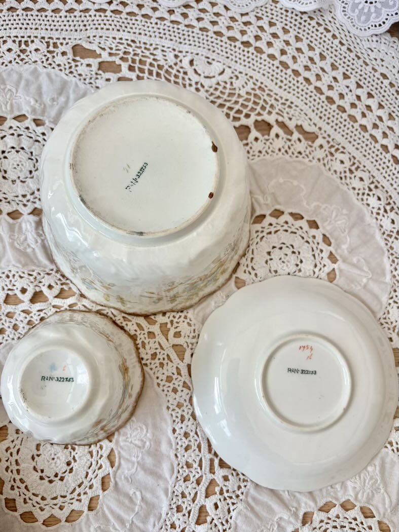 Three white ceramic bowls with visible branding on a lace tablecloth.