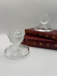 Two clear glass candle holders on a white surface with a book in the background.