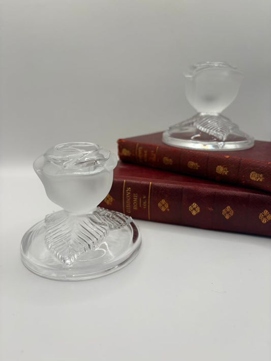 Two clear glass candle holders on a white surface with a book in the background.