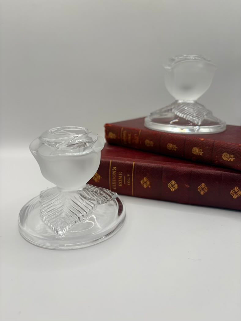 Two clear glass candle holders on a white surface with a book in the background.