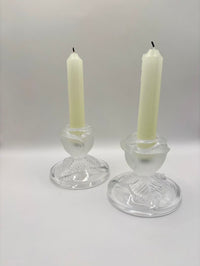 Two glass candle holders with white candles on a white background