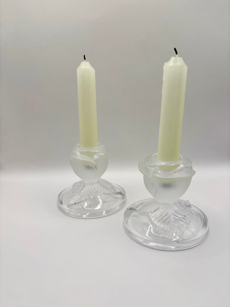 Two glass candle holders with white candles on a white background