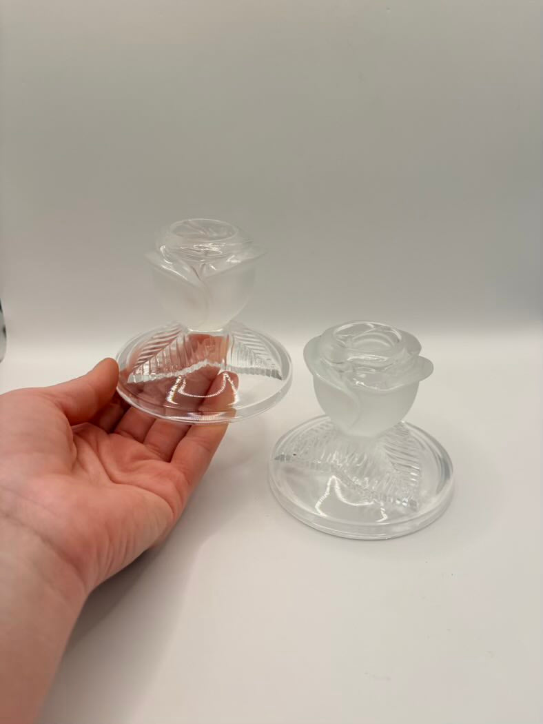 Clear glass candle holders on a white surface with a hand holding one of them.