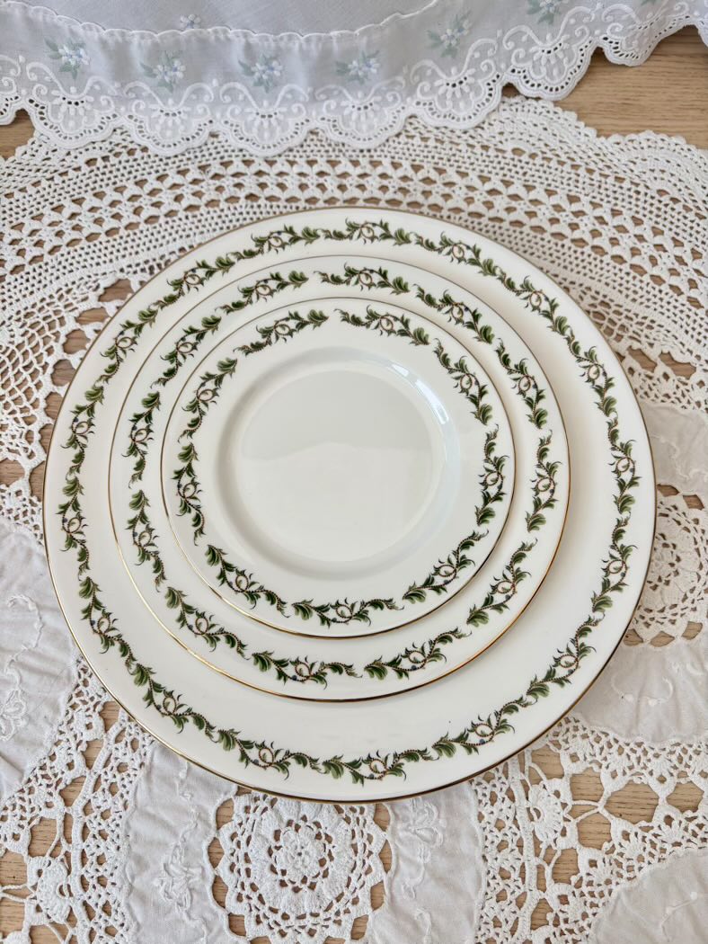 Set of white dinner plates with green floral patterns on a lace tablecloth.