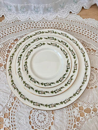Set of white dinner plates with green floral patterns on a lace tablecloth.