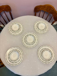 Set of five decorative plates on a round table with a white tablecloth.